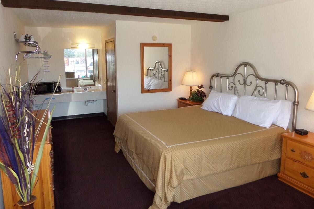 Quarto com cama, mesa de cabeceira, luminária e espelho na parede.