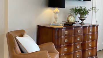 Un sillón de cuero marrón con un cojín blanco, un aparador de madera con varios cajones, un televisor montado en la pared y una planta pequeña sobre el aparador.