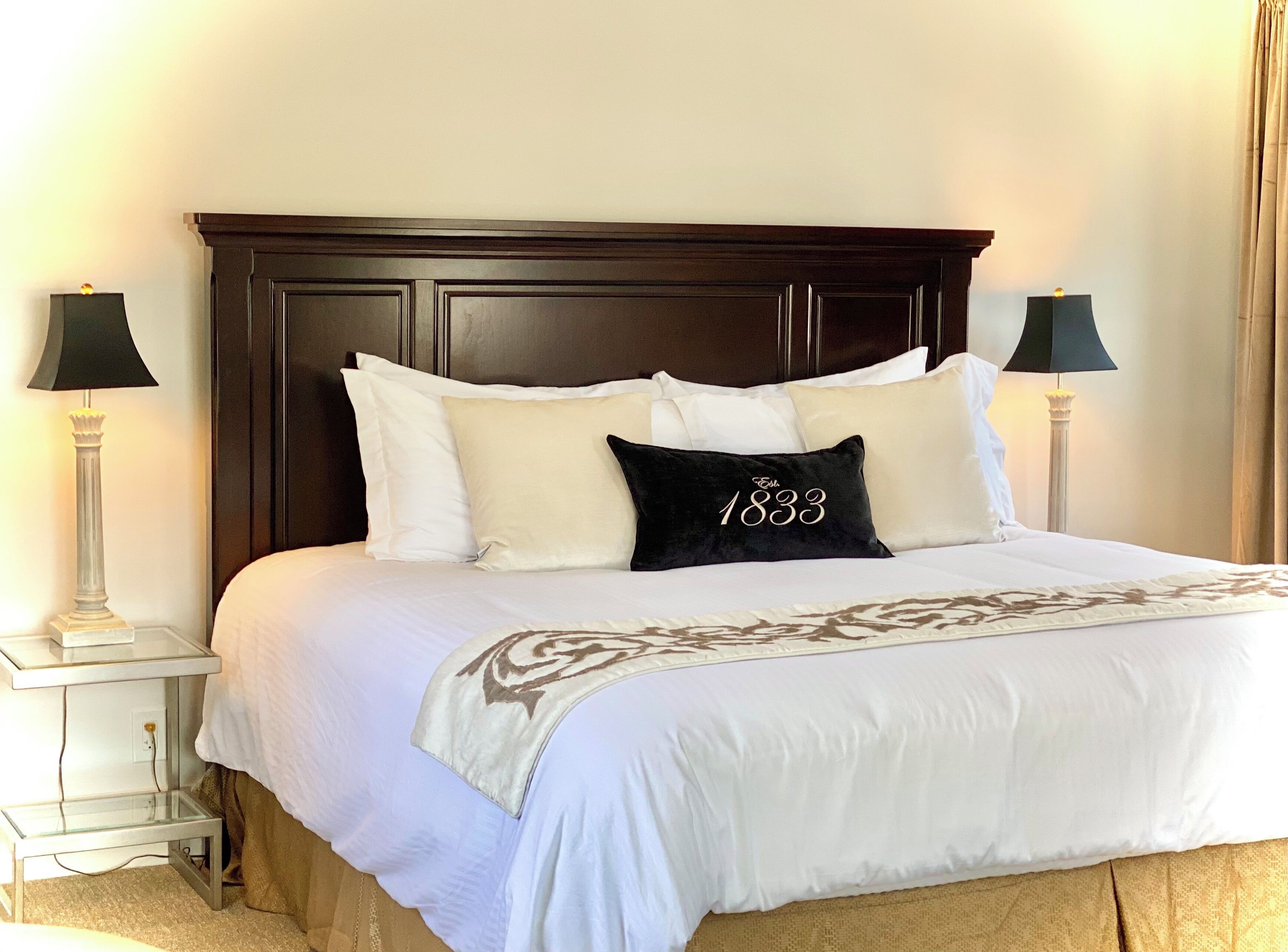 Una cama bien hecha con ropa blanca y una almohada negra con el número '1833' bordado.