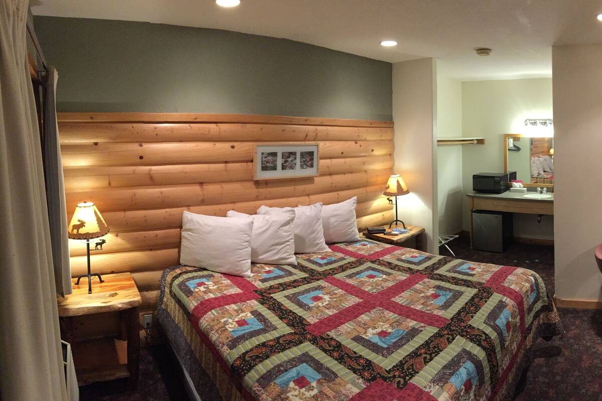Una habitación acogedora con cabecera de madera, colcha acolchada, escritorio con espejo y televisor montado en la pared.