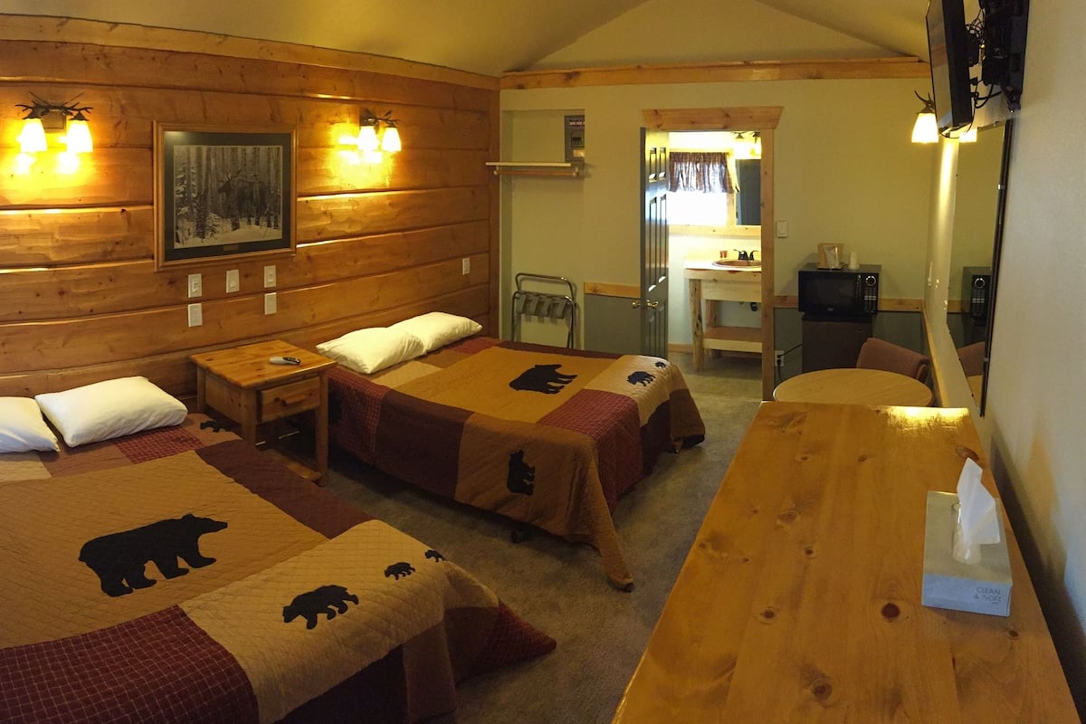 Una habitación tipo cabaña con dos camas, paredes de madera y una mesa de comedor.