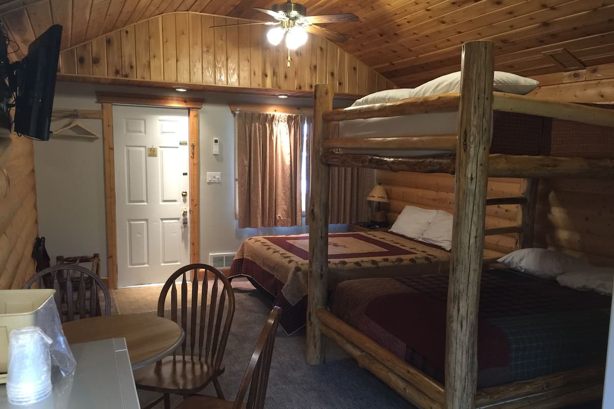 Una habitación tipo cabaña con una cama litera, un escritorio con silla, una mesa y un ventilador de techo.