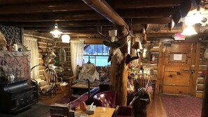 A rustic cabin interior with a wooden dining table, leather chairs, a fireplace, and various hunting trophies. - The Historic Madison Hotel Motel (West Yellowstone)