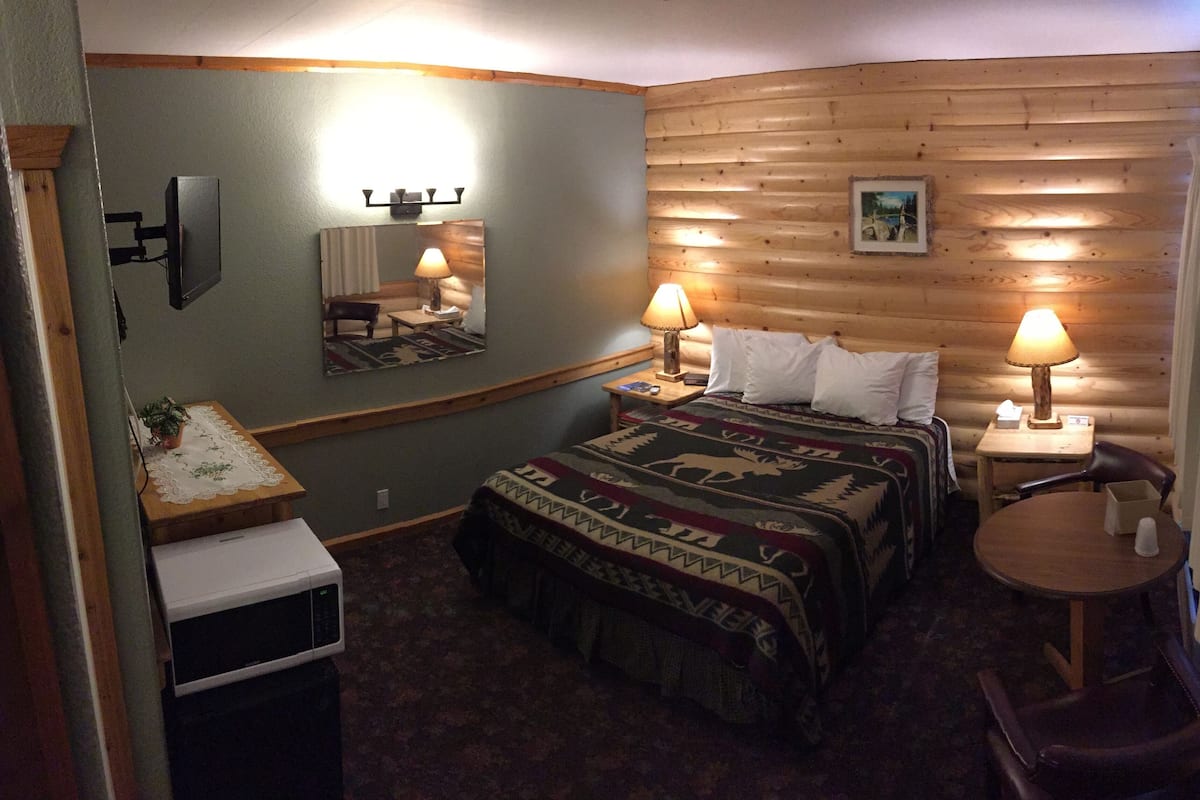 Una habitación acogedora con una cama, dos lámparas de noche, una mesita, una silla y un espejo en la pared.