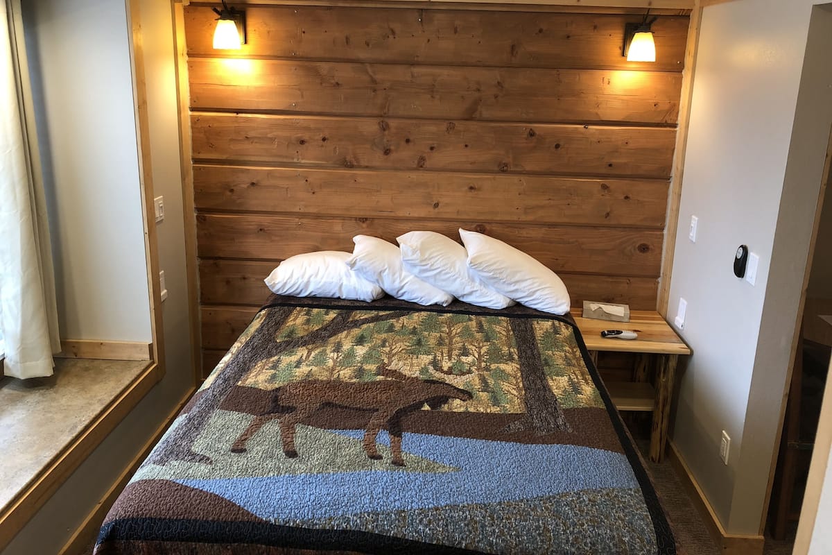 Una habitación con cabecera de madera, una cama con colcha estampada, almohadas blancas y dos lámparas de noche.