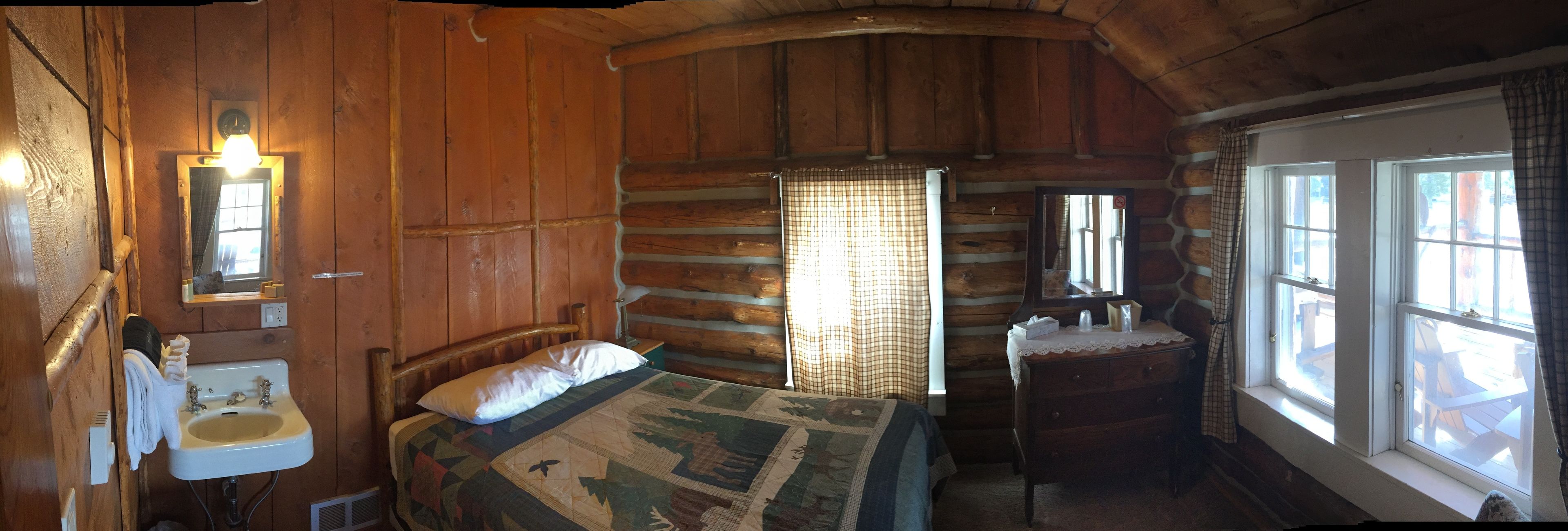 Una habitación rústica de cabaña de troncos con cama, lavabo y ventana con cortinas.