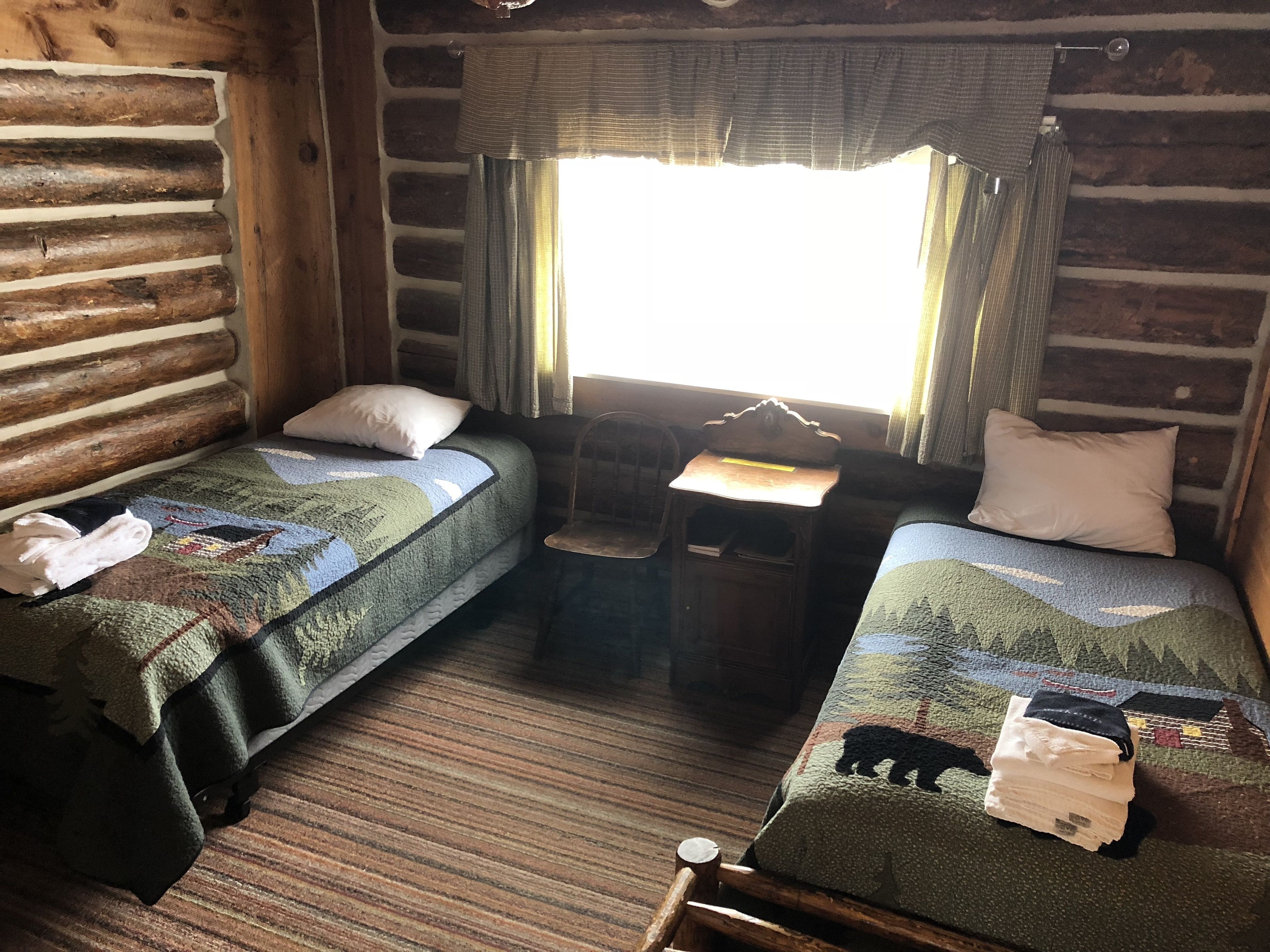 Habitació d'estil cabana amb dos llits individuals, una taula de fusta petita i una finestra amb cortines.