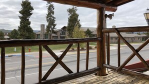 A wooden deck with a railing overlooking a street with a stone building and trees in the background. - The Historic Madison Hotel Motel (West Yellowstone)