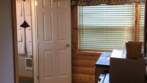 A wooden cabin interior with a door, a window with blinds, a table with a lamp, and two chairs. - The Historic Madison Hotel Motel (West Yellowstone)