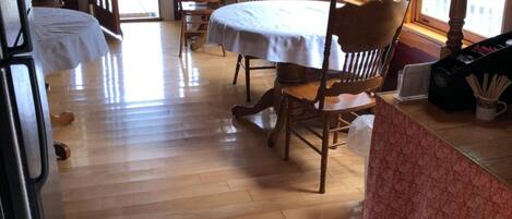 Un comedor de madera con una mesa y sillas, una encimera de cocina y ventanas amplias.