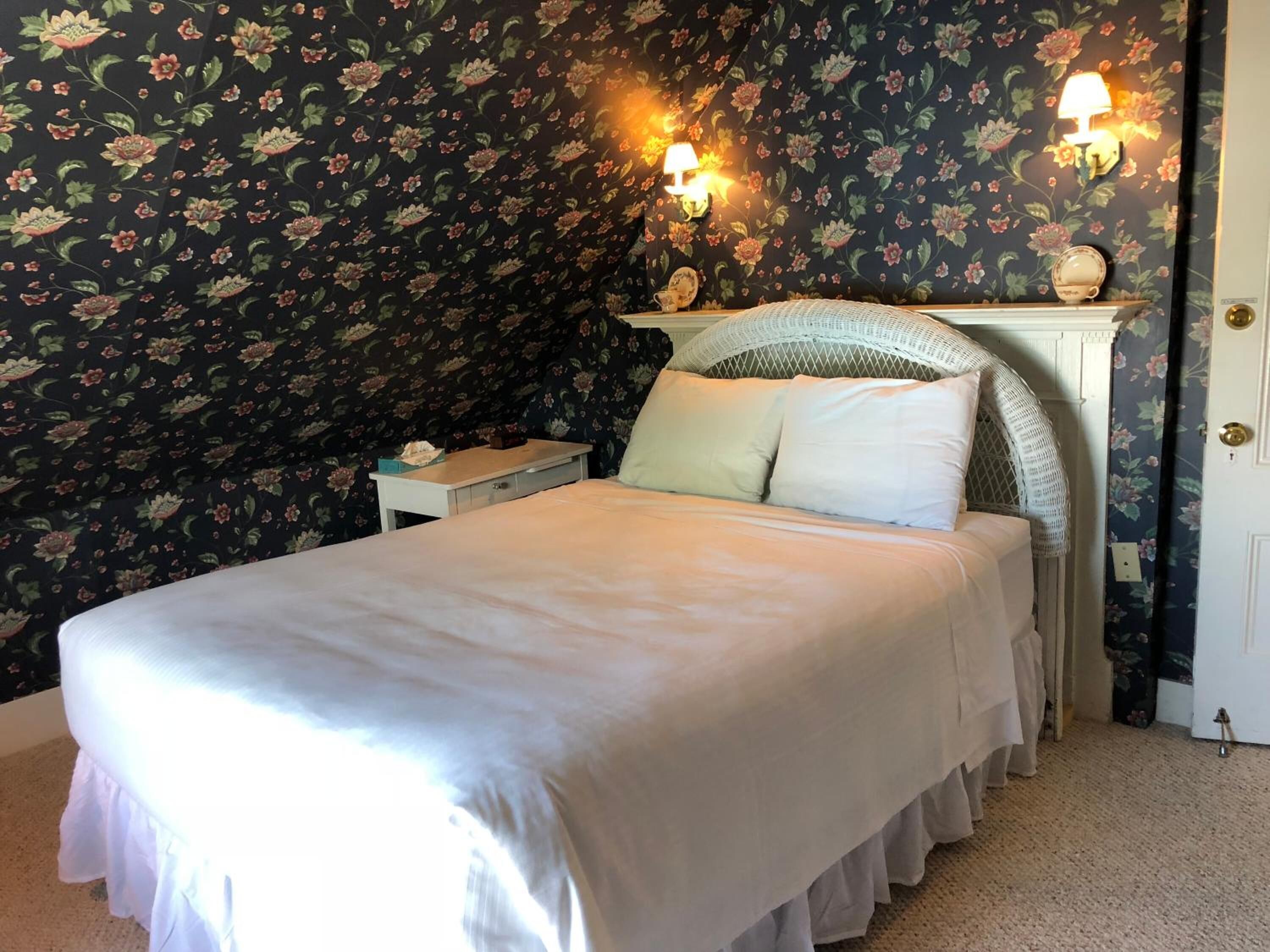A bedroom with a bed, a nightstand, a lamp, and floral wallpaper.