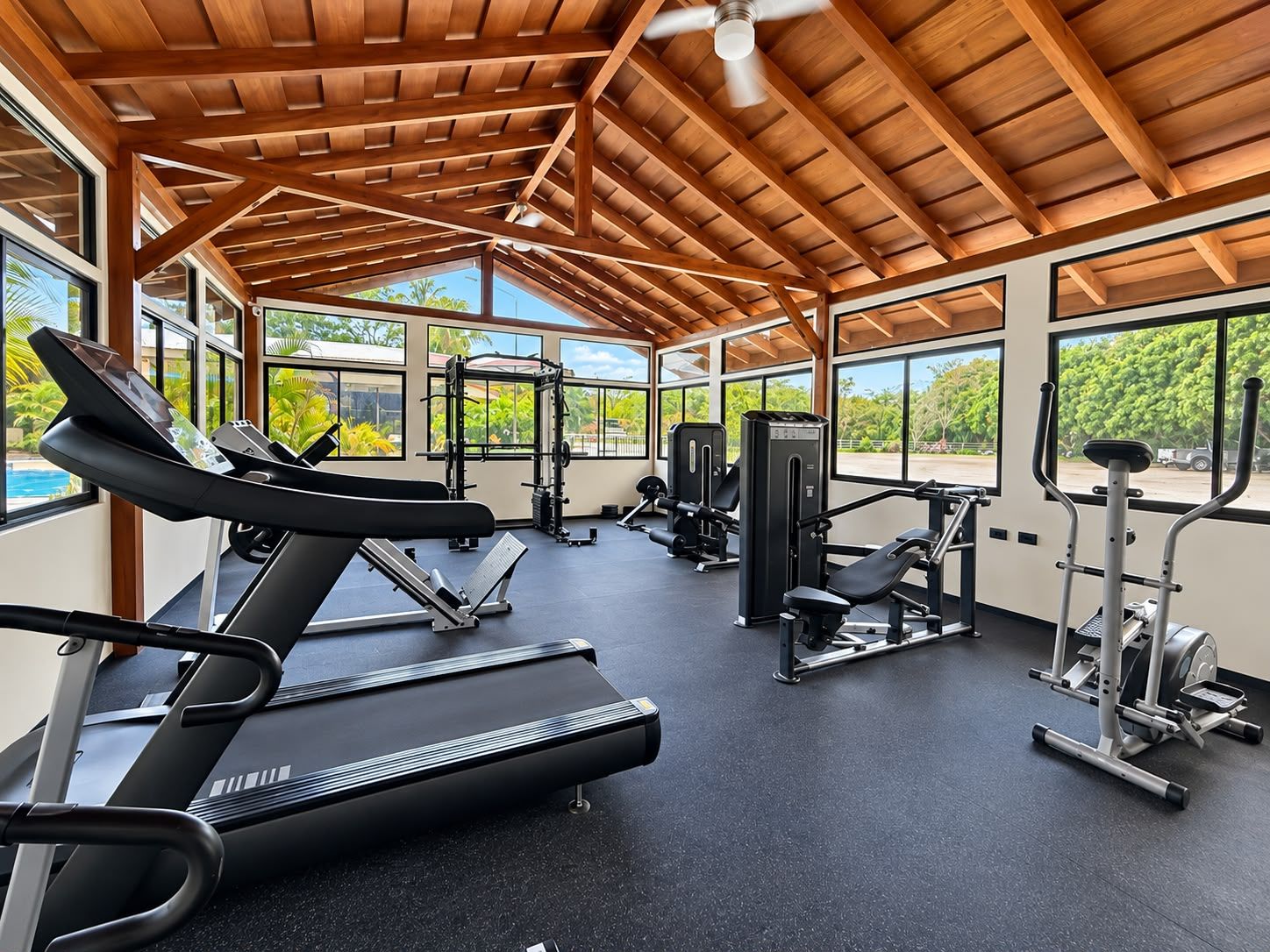 Un gimnasio con cintas de correr, máquinas de pesas y un ventilador de techo.