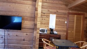 A wooden cabin interior with a TV mounted on the wall, a microwave on a wooden cabinet, a table with chairs, and a door with a sliding glass window. - Rocky Inn (Valemount)