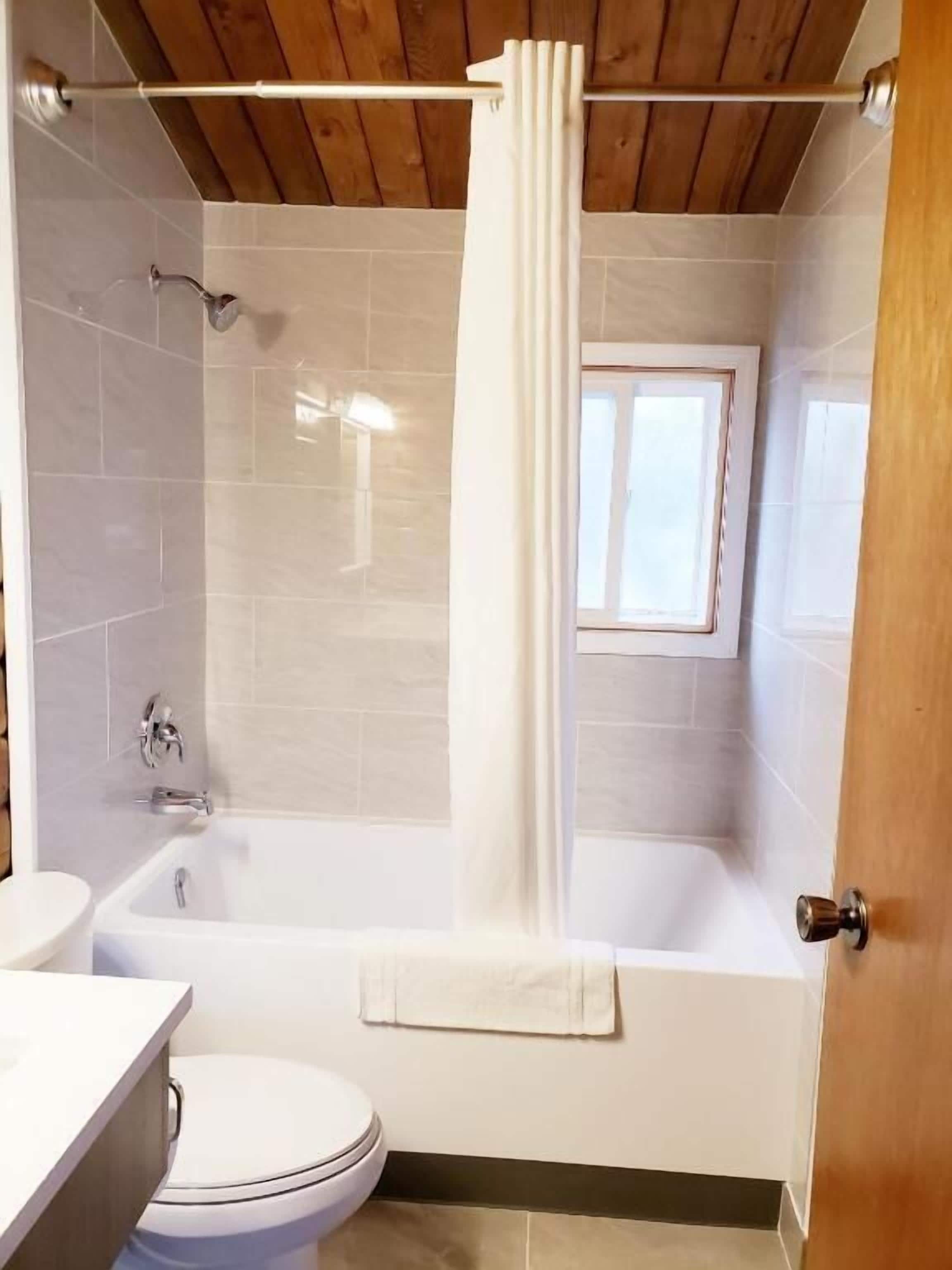 Une salle de bain avec une baignoire, des toilettes et une fenêtre.