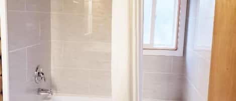 A bathroom with a bathtub, toilet, and a window.