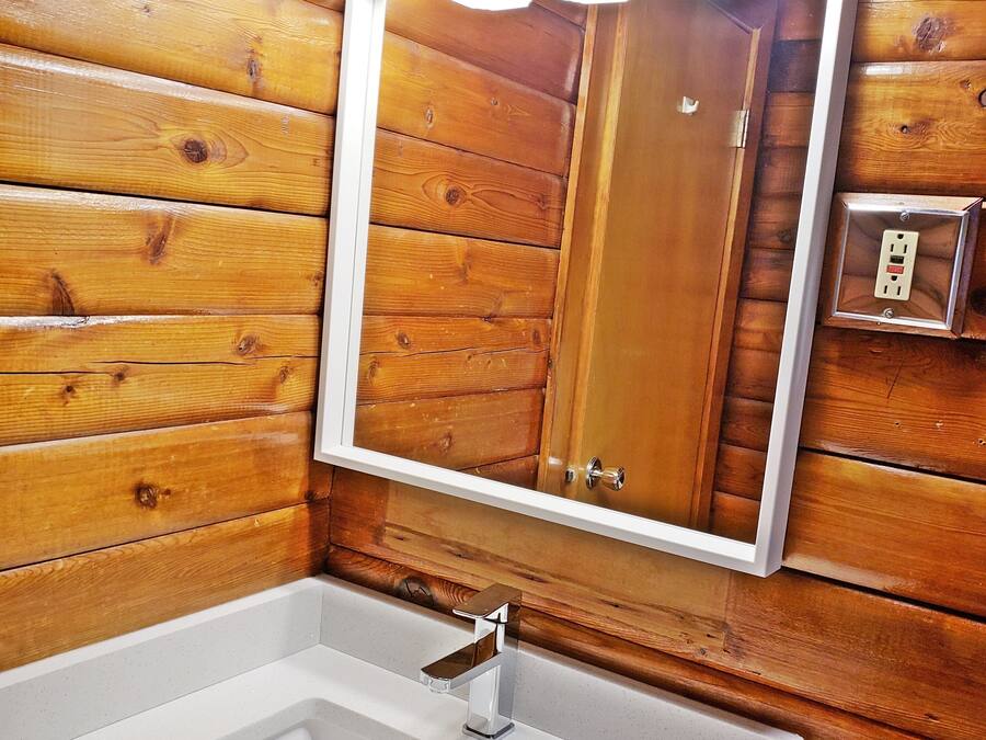 A bathroom with a wooden wall, a white sink, and three overhead lights.