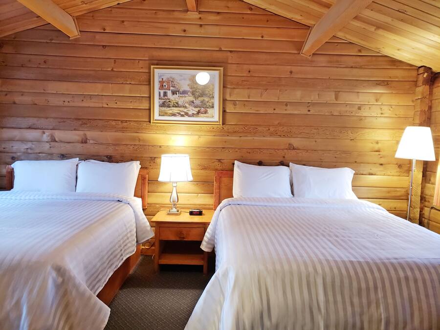 A log cabin room with two beds, a nightstand, a lamp, and a framed picture on the wall.