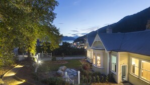 A house with a well-maintained garden, a stone pathway, and a view of a body of water and mountains in the background. - Hulbert House (Queenstown)