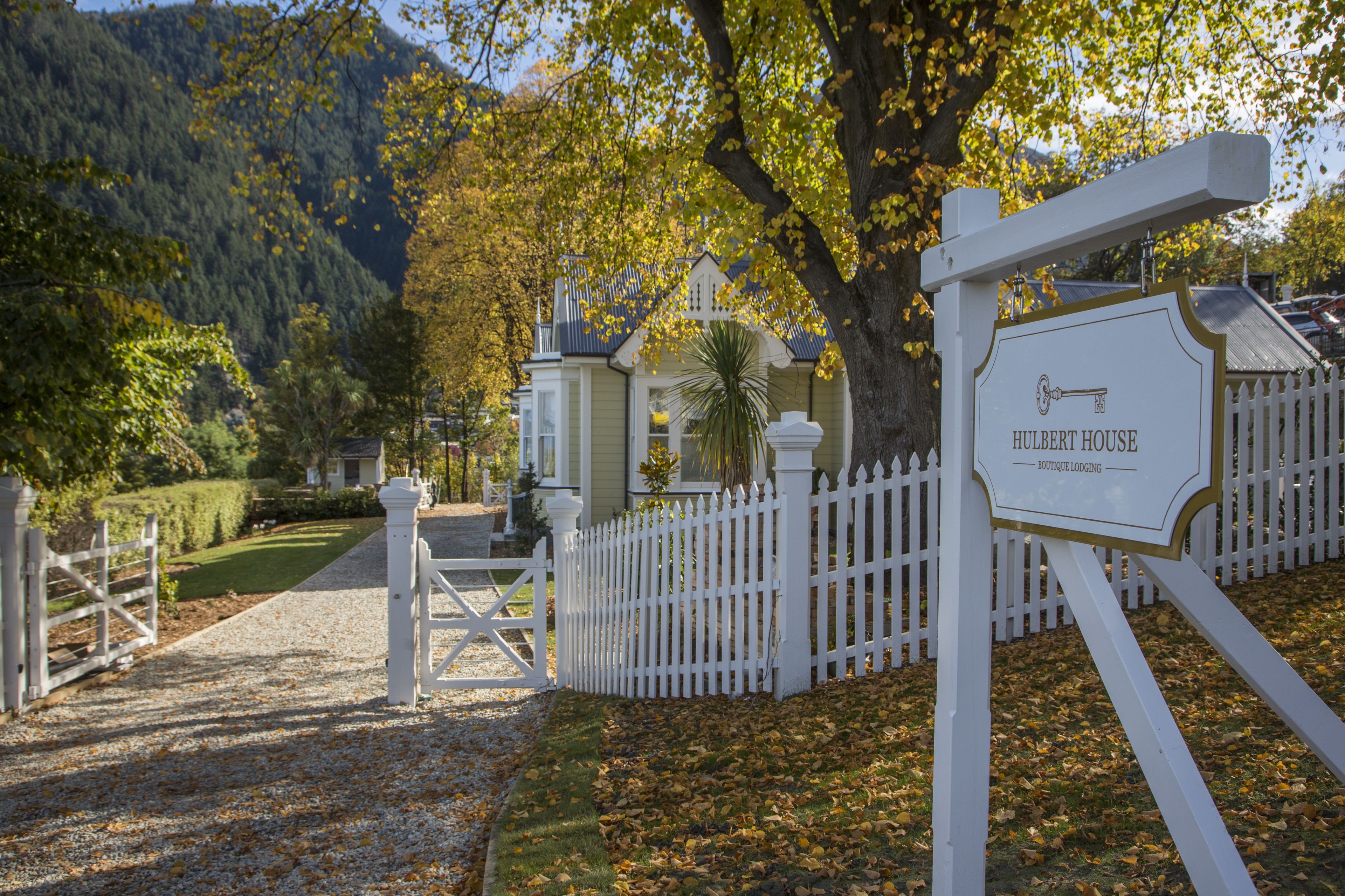 Entrada com portão para um imóvel chamado 'Hulbert House Boutique Lodging', com cerca branca e uma placa.