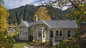 A house with a bay window, a stone pathway, and a view of a forested mountain. - Hulbert House (Queenstown)
