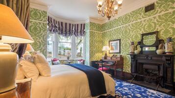 A room with a large bed, a fireplace, a chandelier, and green patterned wallpaper.
