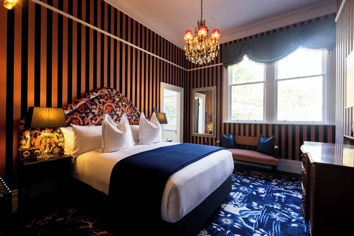 Habitación de hotel con una cama grande, una mesita de noche con lámpara, un aparador y una ventana con cortinas.