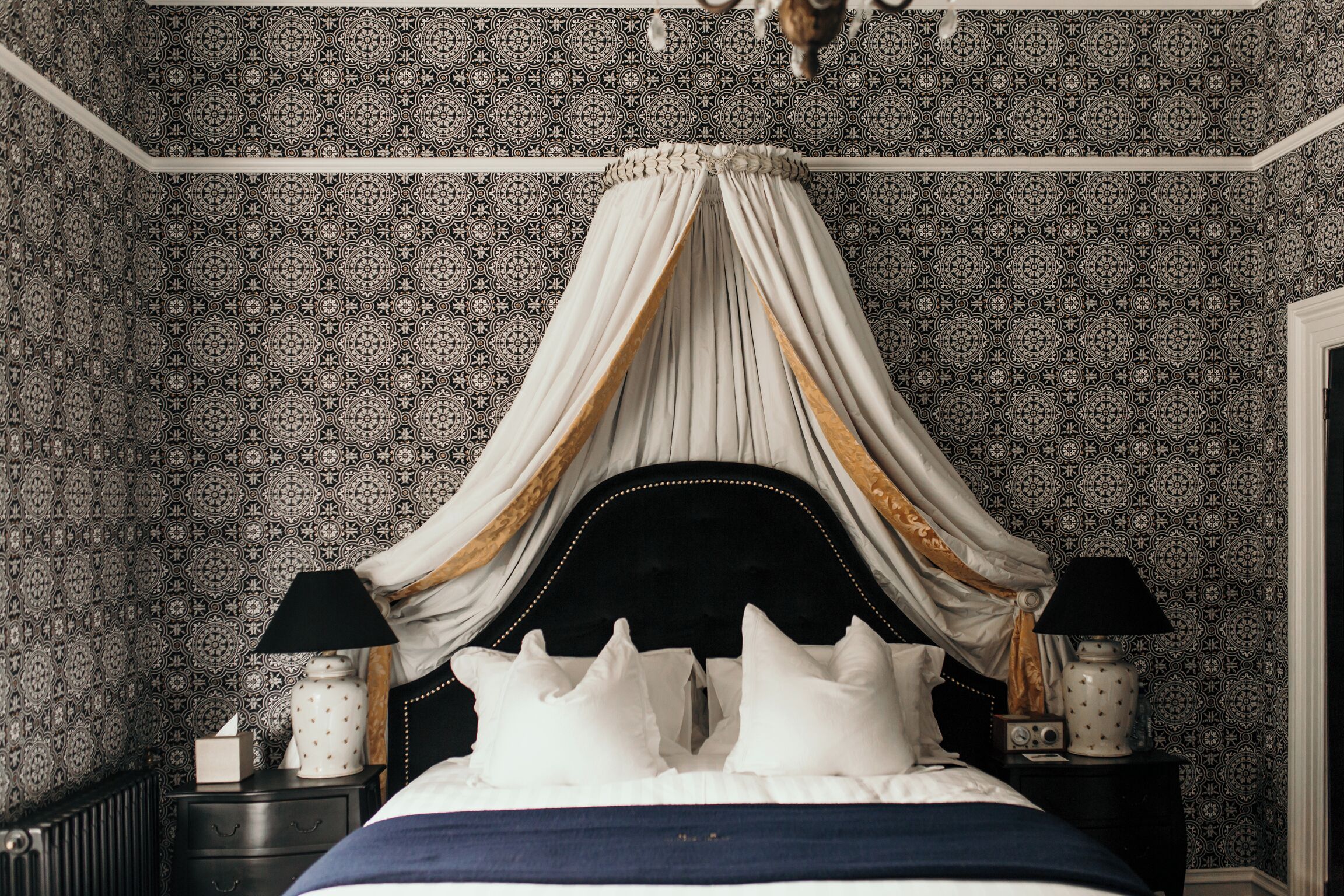 Un dormitorio con cama con dosel, papel tapiz estampado y lámparas de noche.