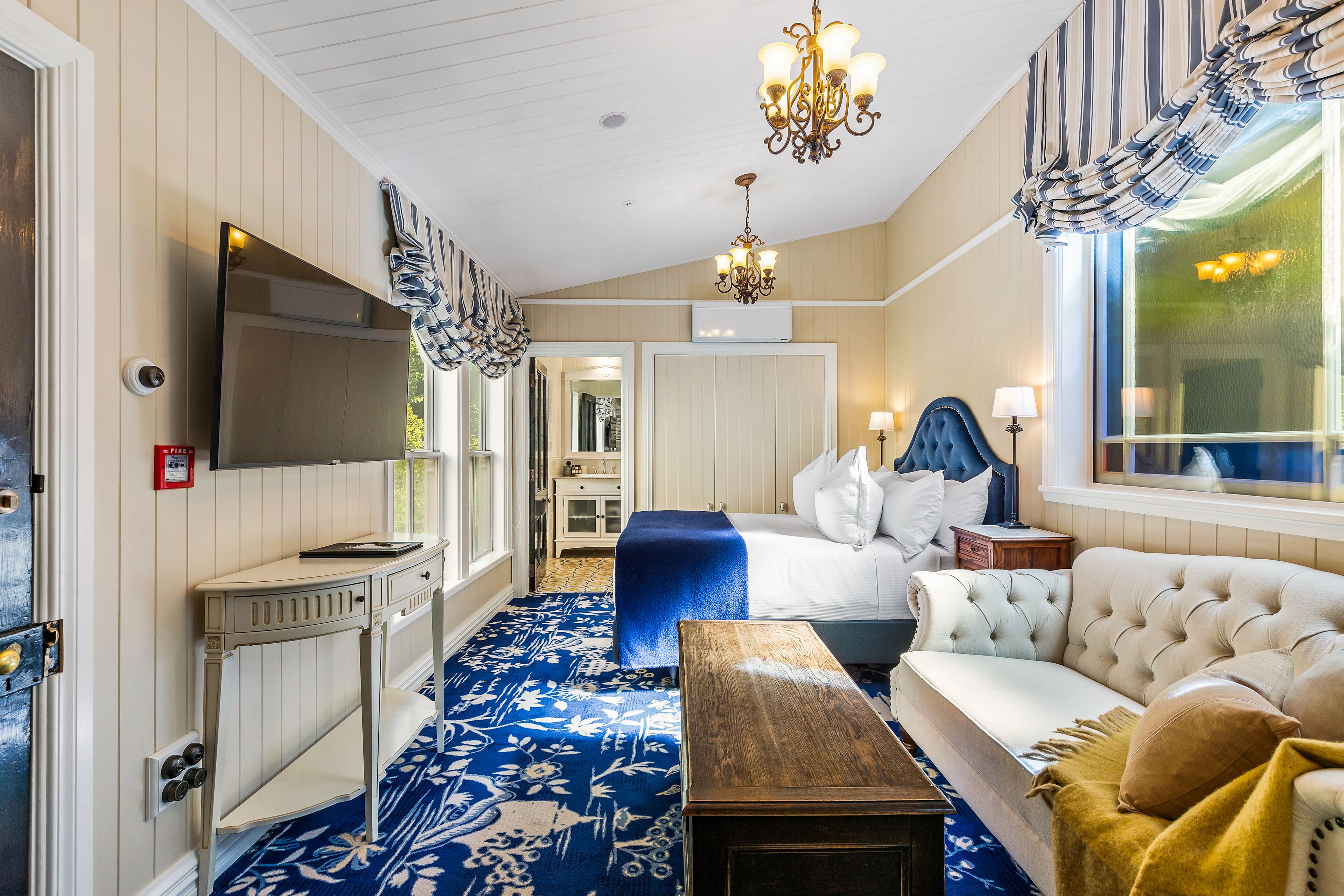 A hotel room with a large bed, a sofa, a desk, and a chandelier.
