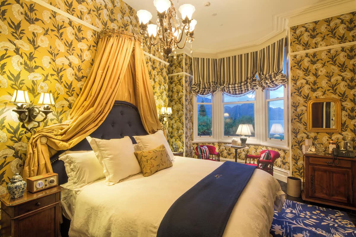 Un dormitorio clásico con cama con dosel, papel tapiz floral y vistas al exterior.