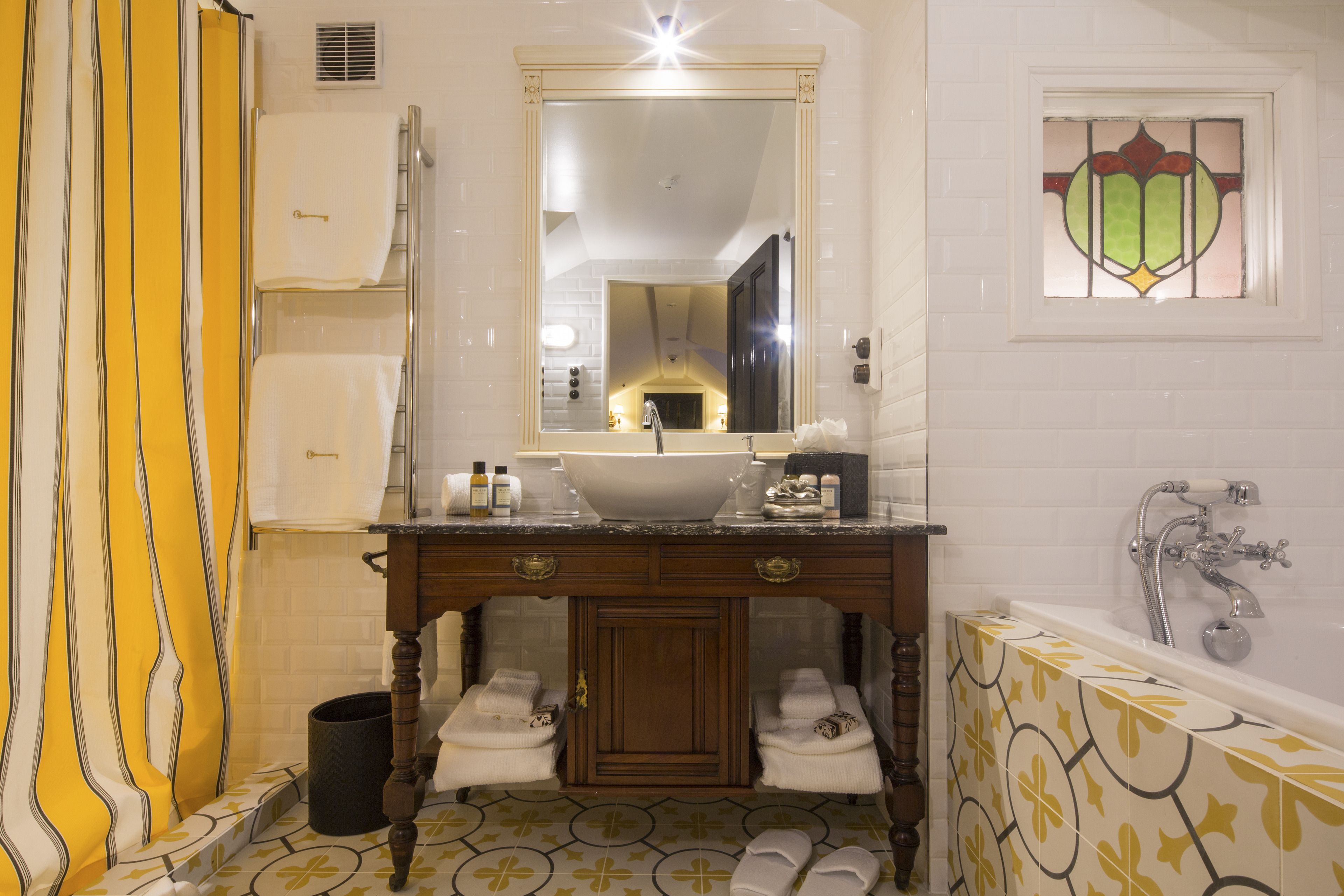 A bathroom with a sink, mirror, and bathtub. There are towels and toiletries on the counter.