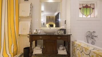 A bathroom with a sink, mirror, and bathtub. There are towels and toiletries on the counter.