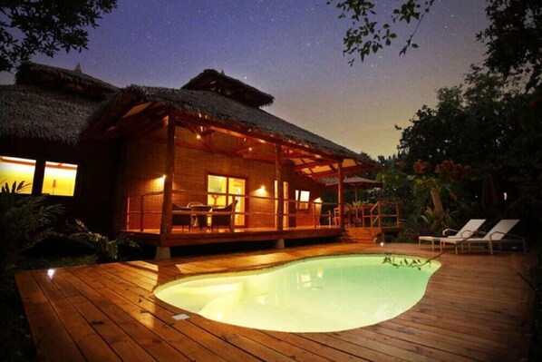 A wooden deck with a swimming pool, a thatched-roof building, and lounge chairs. - Donatela Resort & Sanctuary (Panglao)