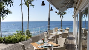 Una terraza con mobiliario de mimbre y una mesa lista para comer, con vista al océano.