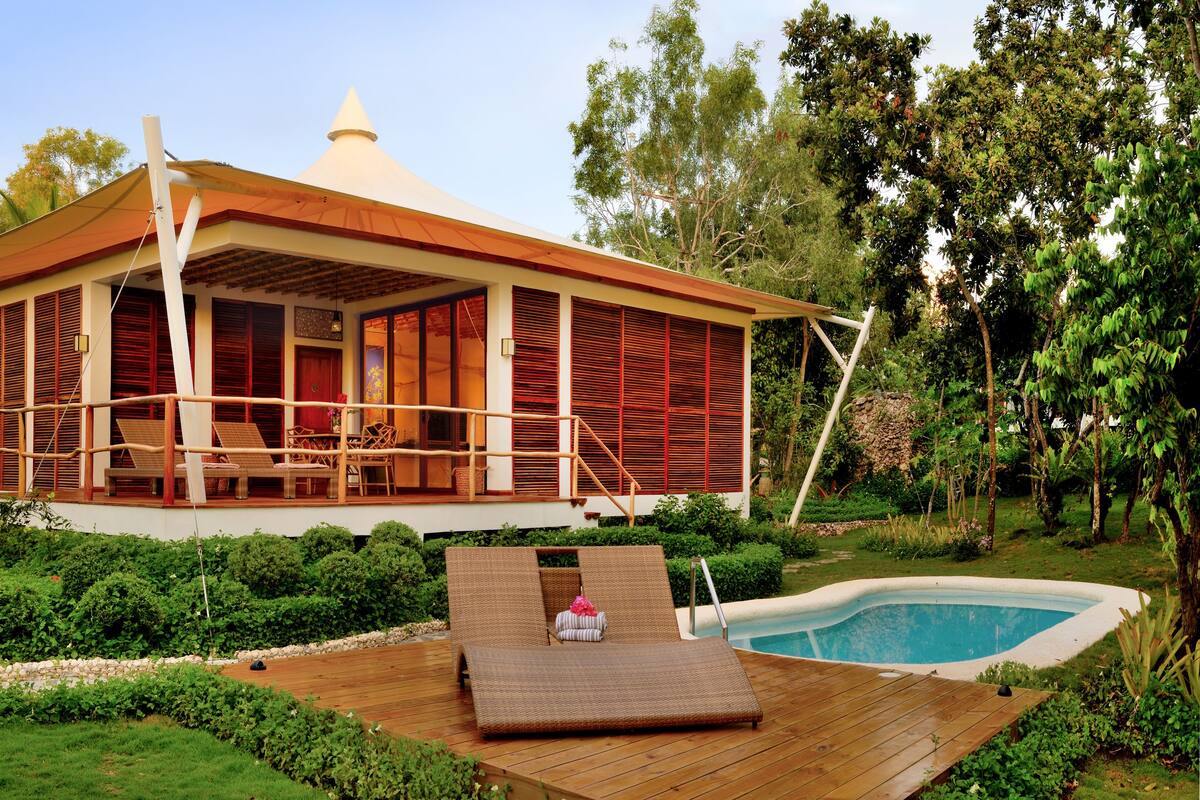 A bungalow with a pool, wooden deck, and lush garden.