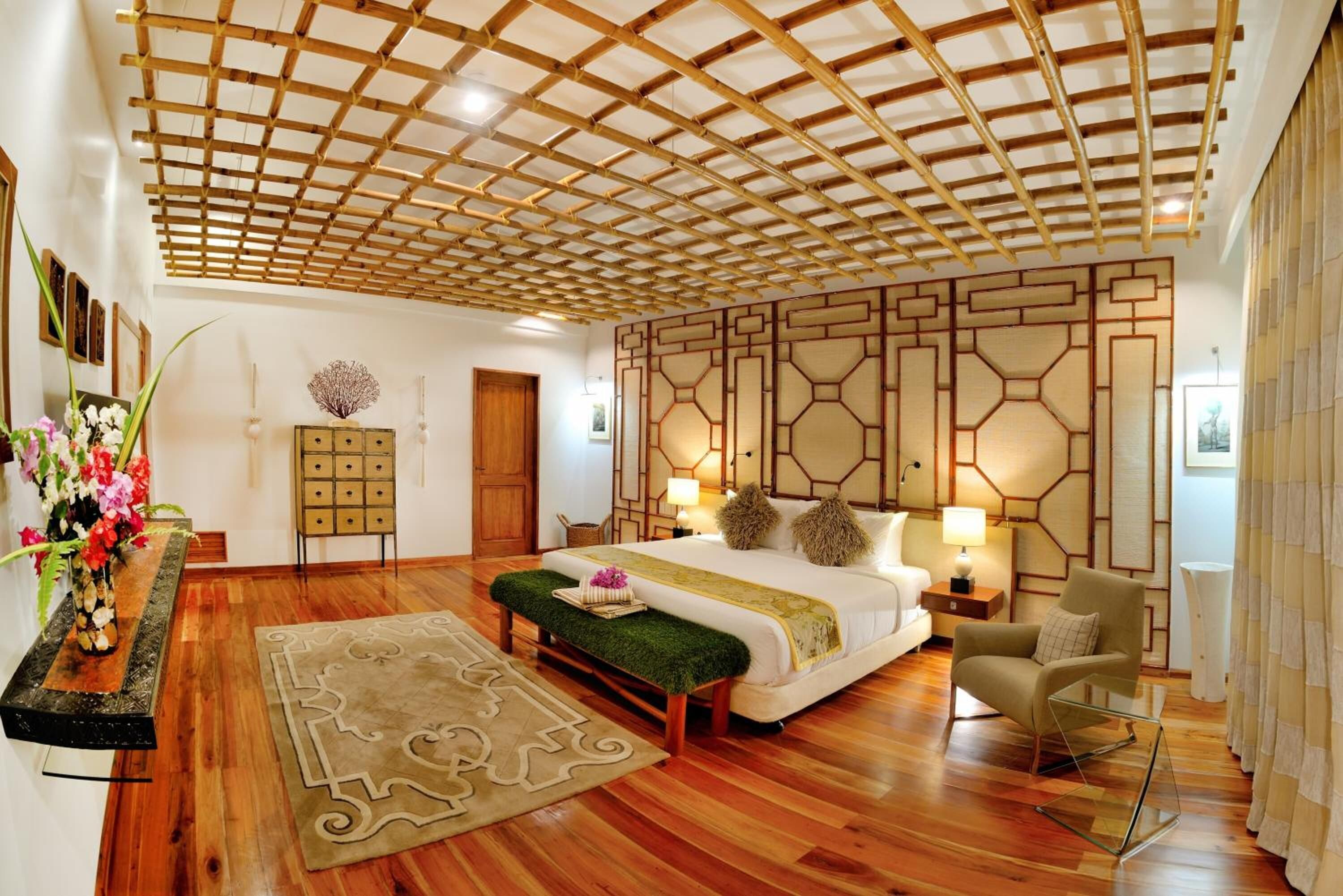 A spacious bedroom with a wooden ceiling, a large bed, a bedside table, a chair, and a decorative wall panel.