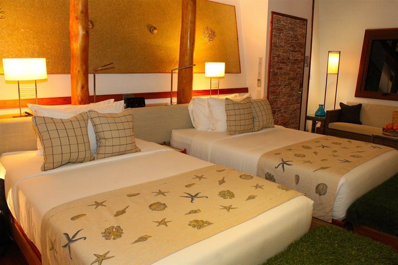 A hotel room with two beds, each with a sea-themed bedspread, a wooden headboard, and a nightstand with a lamp.