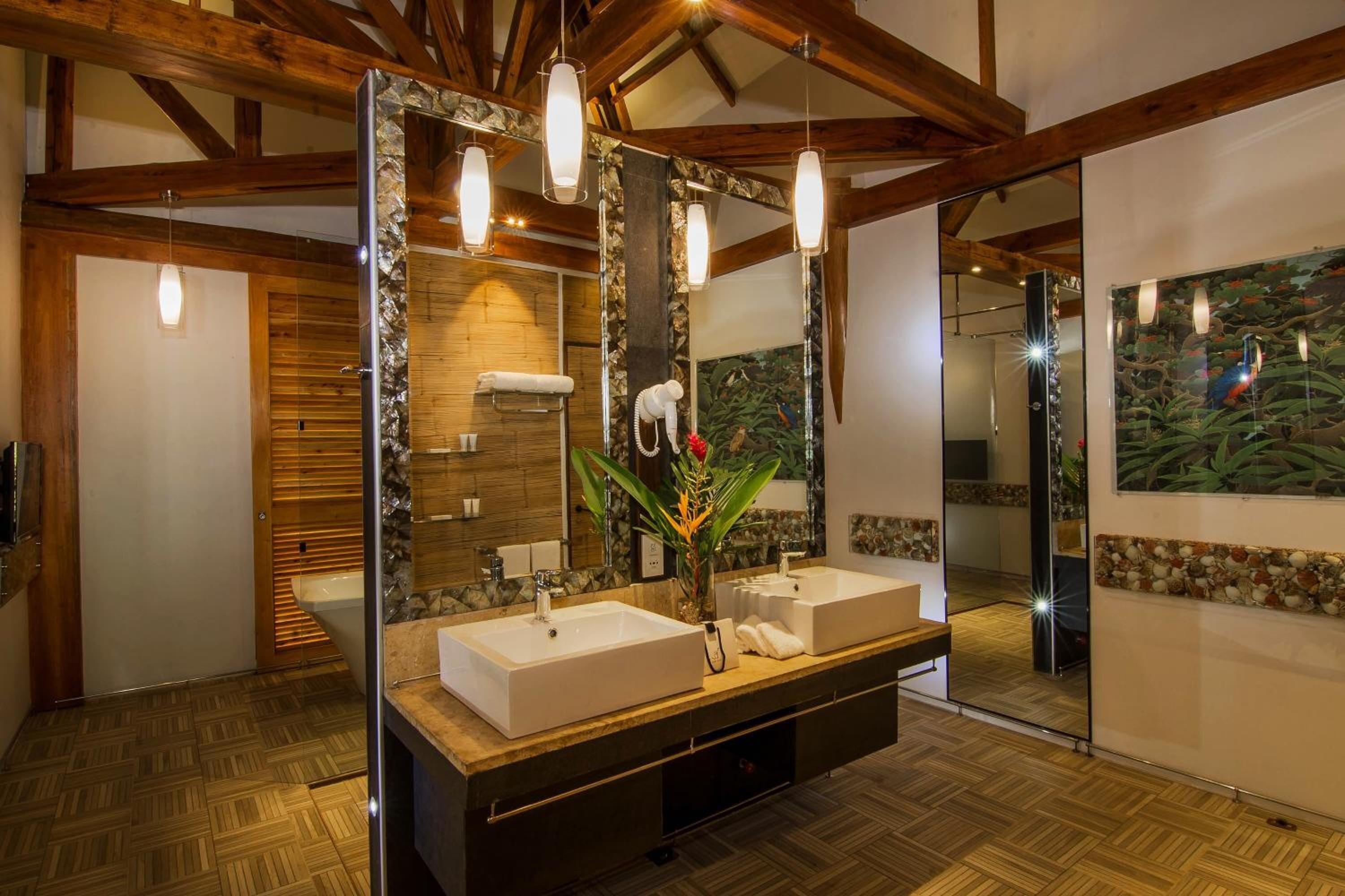 Baño con tocador de madera, dos lavamanos, un espejo y zona de ducha.