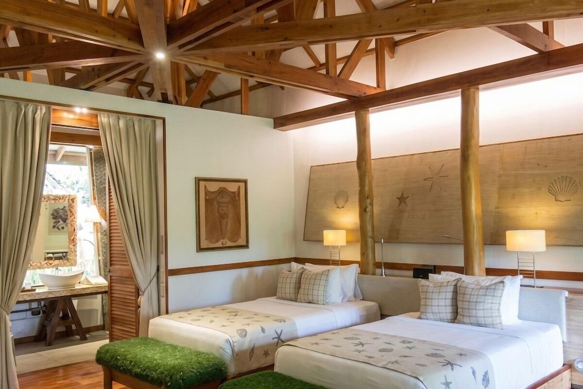 Una habitación con dos camas, vigas de madera, un escritorio con lámpara y una obra de arte en la pared.