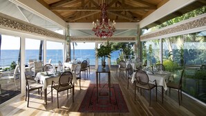 Un comedor amplio con vista al océano, techo de madera y una araña.