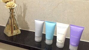 A bathroom shelf with a vase of dried flowers and four bottles of Aromatherapy Associates products. - 3D Inn - Romance (Kowloon)
