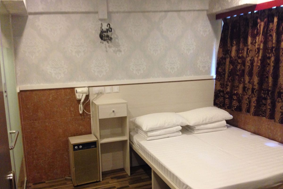 A hotel room with a single bed, a bedside table, a small drawer unit, and a wall-mounted telephone.
