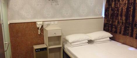 Quarto de hotel com uma cama de solteiro, mesa de cabeceira, pequeno móvel com gavetas e telefone fixado na parede.