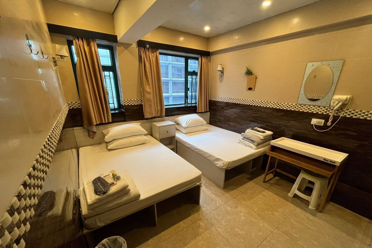 A hotel room with two beds, a small bedside table, a mirror, a telephone, and a window with curtains.