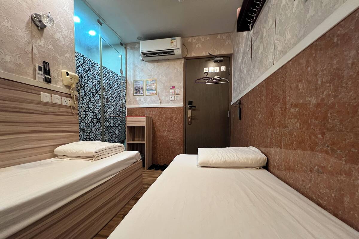 A hotel room with two beds, a wooden headboard, a small shelf, and a door leading to a bathroom.