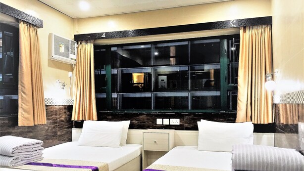 A hotel room with two beds, a large window with curtains, a wall-mounted air conditioner, and a small bedside table. - 3D Inn - Romance (Kowloon)