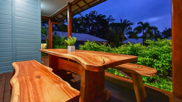 A wooden deck with a table and benches, surrounded by lush greenery and a view of palm trees. - Blue Summit Hideaway (Yungaburra)