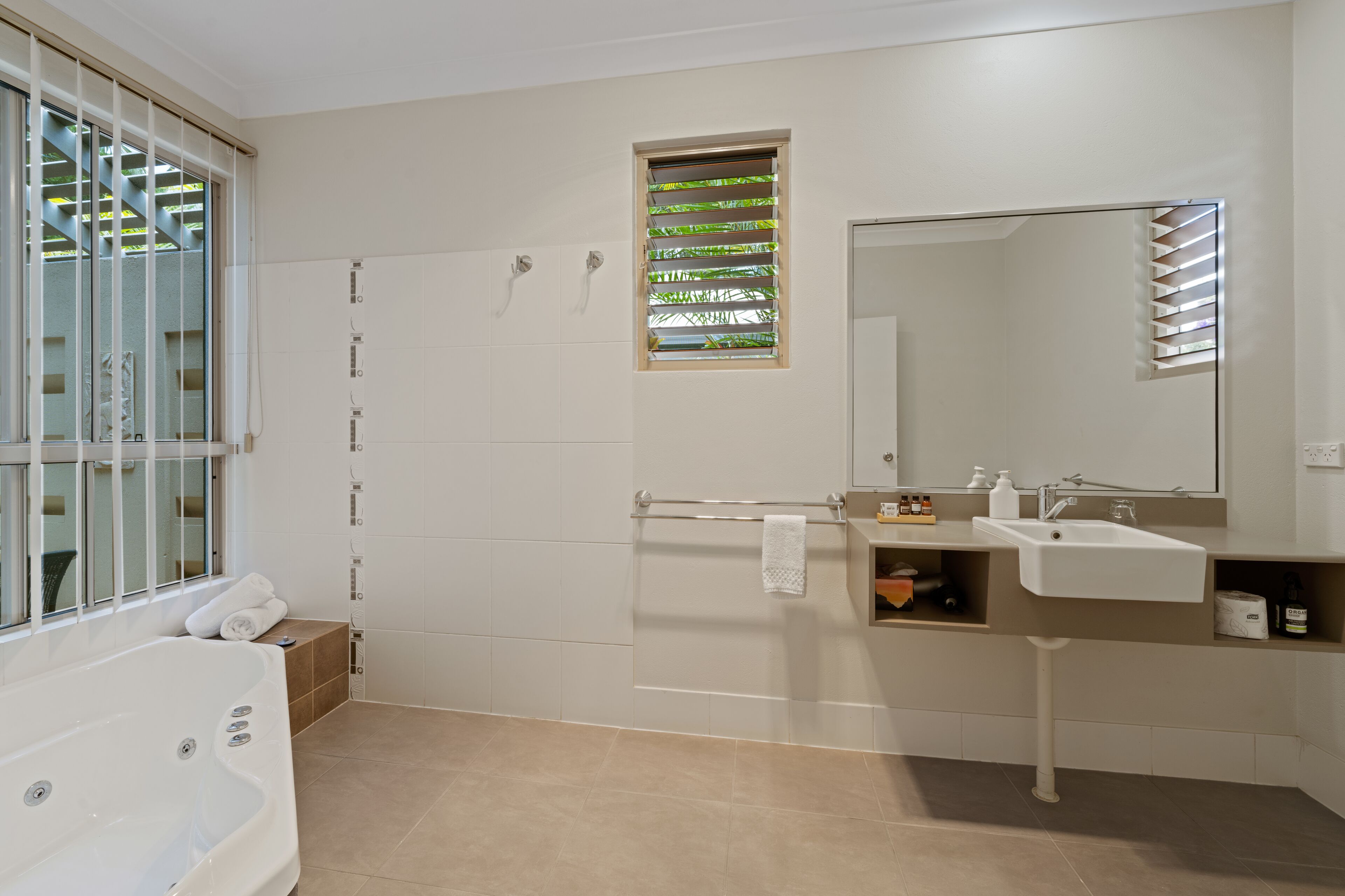 A modern bathroom with a bathtub, a vanity with a mirror, and a window with blinds.