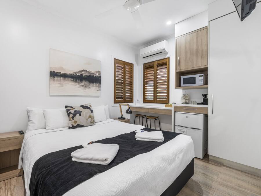 Un dormitorio moderno con cama, mesitas de noche, un escritorio y un microondas.