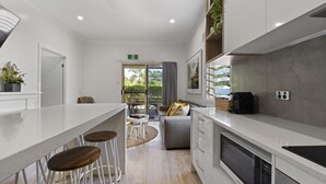 A modern kitchen with a white countertop, wooden stools, and a dining area with a table and chairs. - Blue Summit Hideaway (Yungaburra)