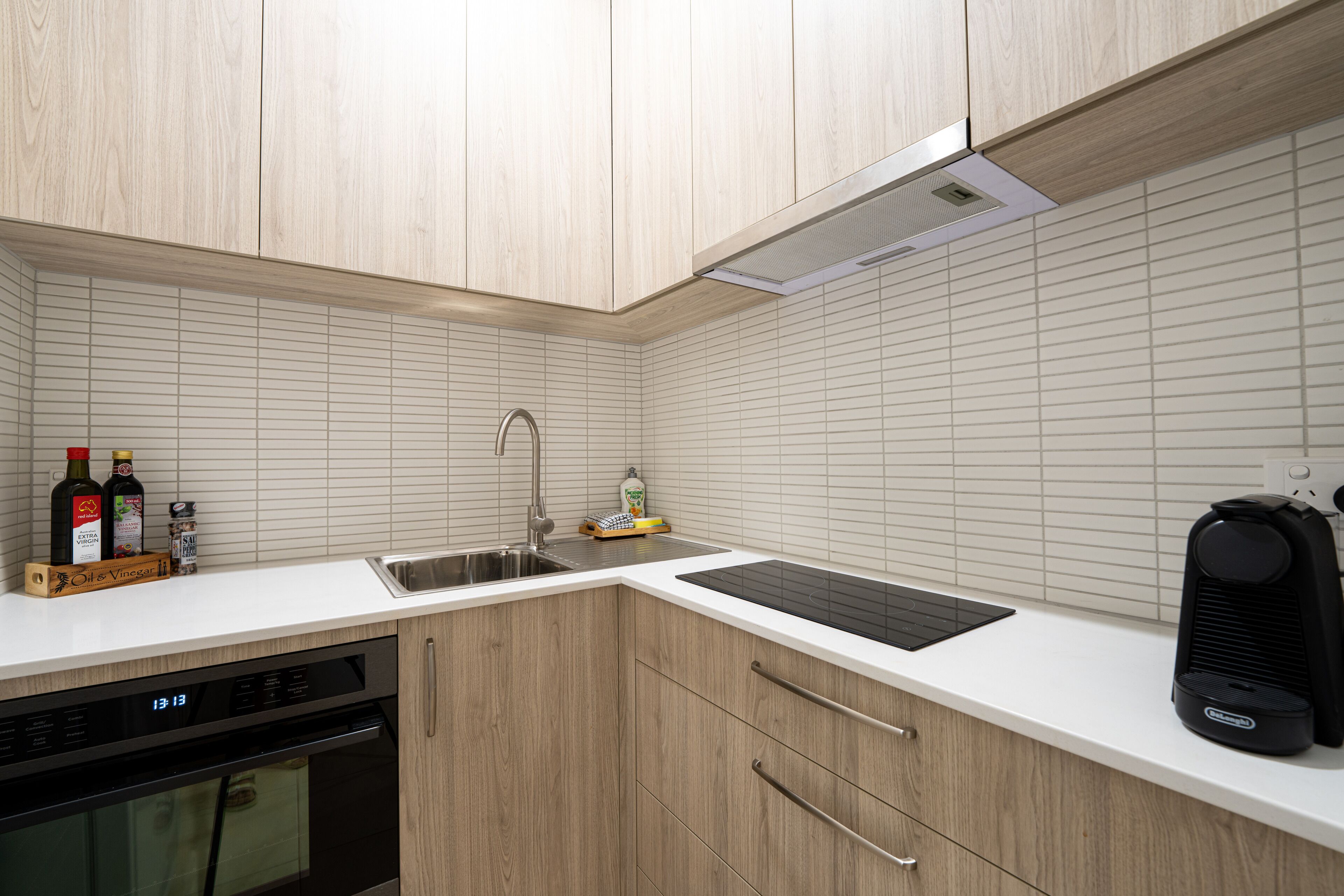 Una cocina con armarios de madera, encimera blanca, lavavajillas empotrado y cafetera.